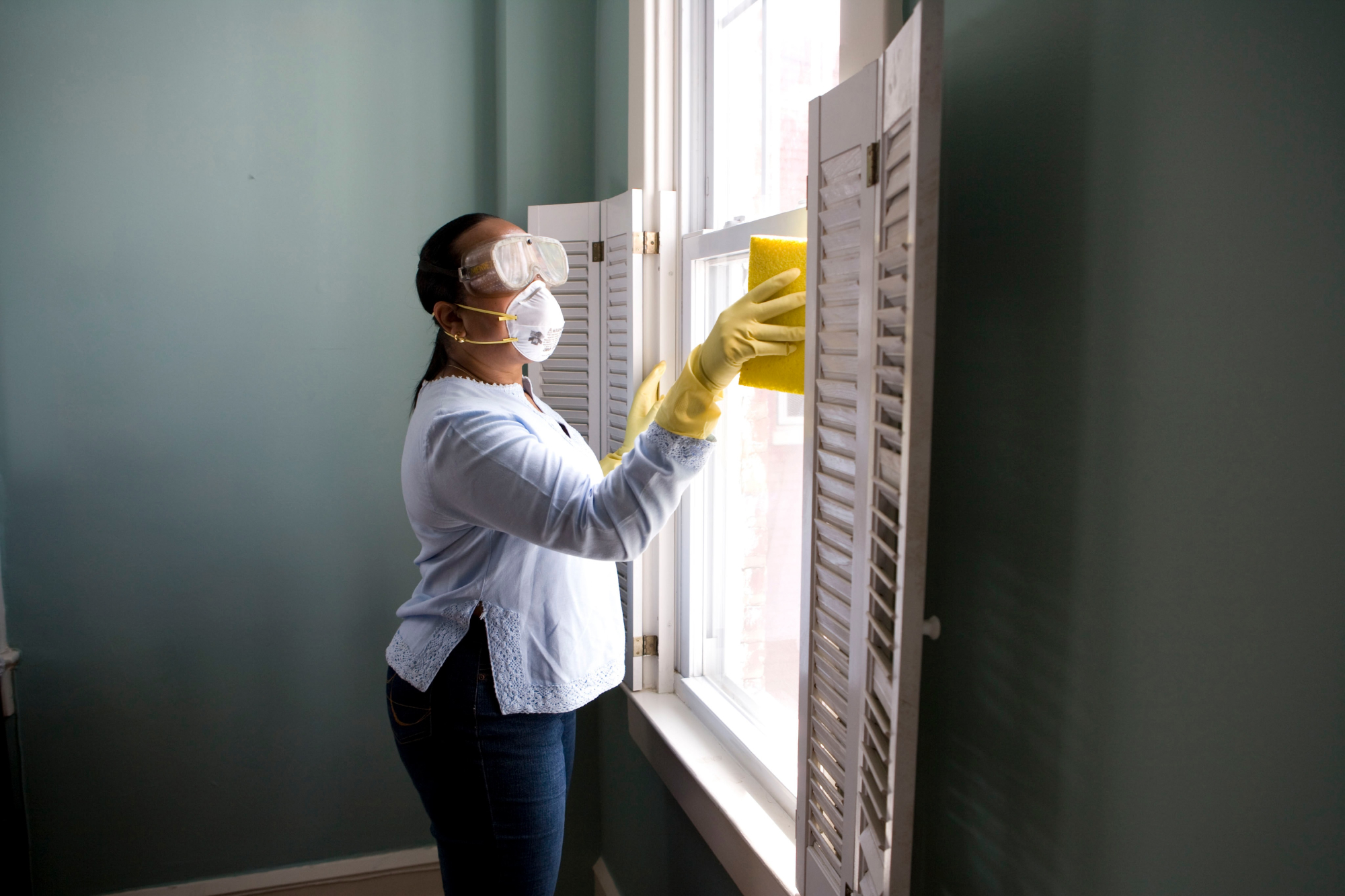 A cleaning lady wearing a protective mask, safety goggles and rubber gloves